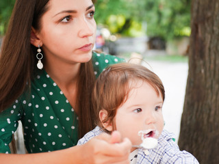 mom feeds her baby on the street. A mother feeds her little baby with a spoon on the street. mouth...