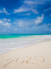 Fototapeta na wymiar New Year 2020 handwritten on the sandy beach with ocean wave