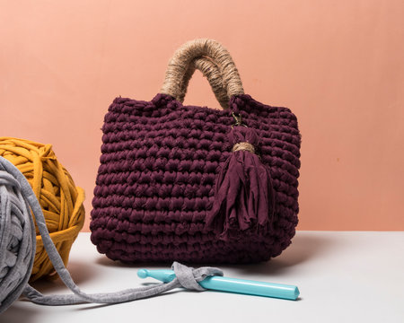 Bolso vinotinto y beige hecho a mano con trapillo junto a bolas de tela de trapillo de colores