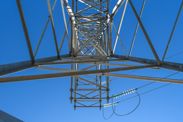 Supports high-voltage power lines against the blue sky. View from the bottom up