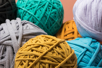 Bolas de trapillo de colores azules, amarillo beige y cafés sobre un fondo color  coral por...