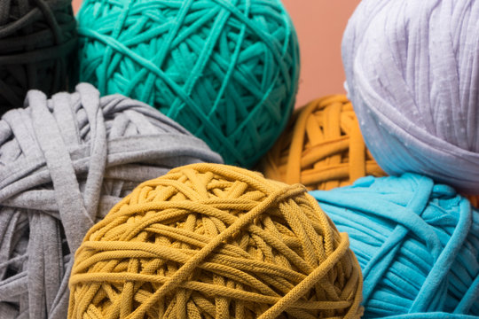Bolas de trapillo de colores azules, amarillo beige y caf&eacute;s sobre un fondo color  coral por montones