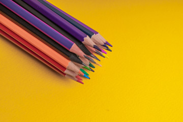Many sharpened colored pencils laid out on a yellow background. Copyspace.