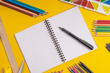 School supplies laid out on a table. Copy space in the form of an open notebook with an ink pen on it. Horizontal image.