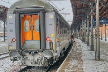 Fototapeta na wymiar last car in the train on the platform, rail travel in winter, train punctuality and lateness, woman getting on the train, snow-covered railway carriage
