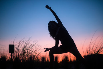 The silhouette of an unrecognizable woman practicing tai chi, yoga and minfulness at sunset