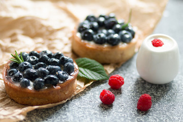 Delicious blueberry tartalets with vanilla cream and with raspberry on a black and white plate on a grey background.