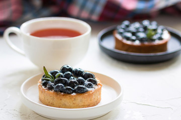 Delicious blueberry tartlets with vanilla custard cream on a black and white plates with a cup of tea 