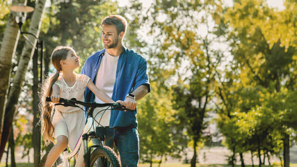Cute smiling girl learning to ride a bicycle with her father outdoors