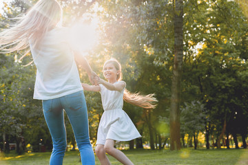 Mother and little daughter dancing, having fun in a park - obrazy, fototapety, plakaty
