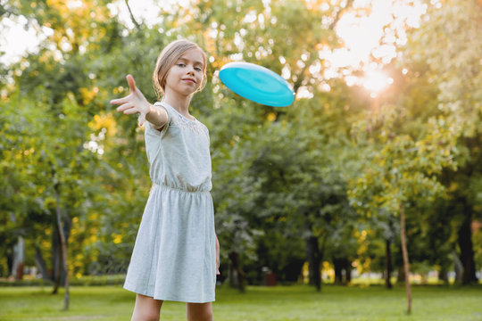 Cute smiling little girl playing frisby and having fun in city park