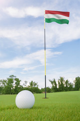 Obraz premium Hungary flag on golf course putting green with a ball near the hole