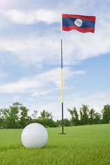 Obraz premium Laos flag on golf course putting green with a ball near the hole