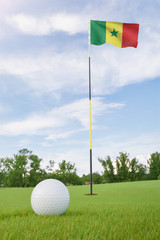Obraz premium Senegal flag on golf course putting green with a ball near the hole