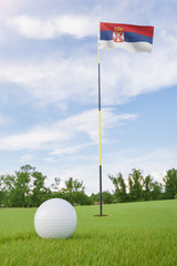 Obraz premium Serbia flag on golf course putting green with a ball near the hole