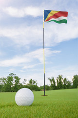 Obraz premium Seychelles flag on golf course putting green with a ball near the hole