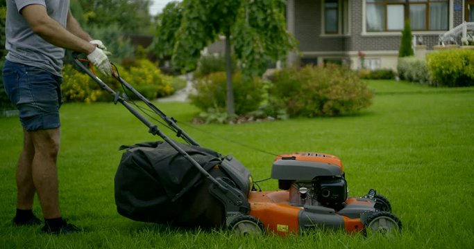 man in grey t-shirt starts lawn mower on grass slow motion