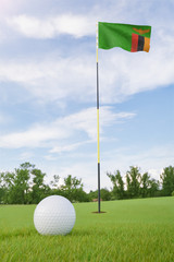 Obraz premium Zambia flag on golf course putting green with a ball near the hole