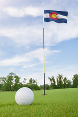 Obraz premium Colorado flag on golf course putting green with a ball near the hole