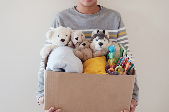 Young volunteer preteen teenage boy holding a box full of used toys, cloths, books and stationery for donation