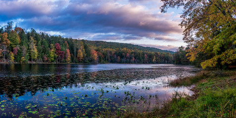Pink and purple clouds hover over the fall colors around the lake shore and are being reflected by...
