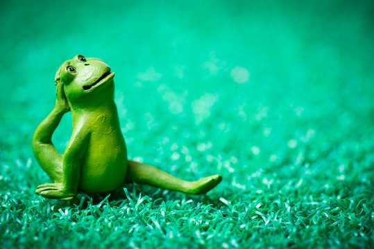 Cute little wooden frog doing yoga poses on a green grass like mat.
