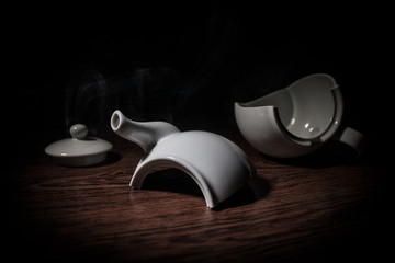 broken teapot on a dark toned foggy background. Pieces of ceramic teapot on wooden table.