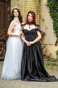 Two Girls Together Standing Embraced Outdoors. Posing in Black and White Dresses.  Wearing Diadems.