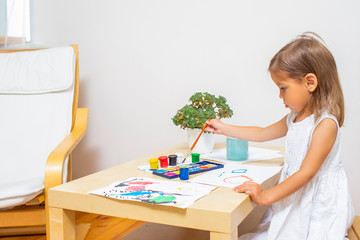 Caucasian Blond Girl Drawing Using Brushes and Paint at Table.