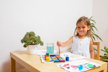 Funny Smiling Little Caucasian Blond Girl Drawing Using Brushes and Paint at Table.