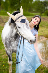 Caucasian Brunette With Tiara Walking with Horse Outdoors. Against Nature Background.