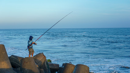man fishing on the edge of the blue sea