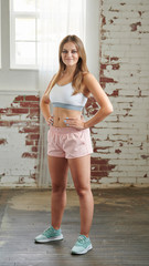 Beautiful young blonde fitness model poses in sports bra and pink shorts