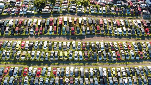 Rising aerial shot revealing rows of hundreds of colorful wrecked cars in vehicle salvage junkyard in afternoon sunlight