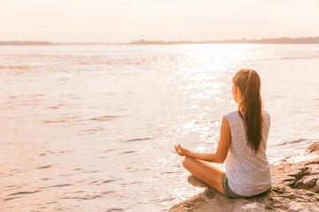 Yoga healthy woman meditating on morning sunrise by the lake. Beach meditation wellness girl enjoying summer sunshine.