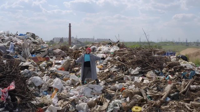 Aerial shot of tramp woman standing at peak of city dump mountain. homeless person is happy on trash mount.
