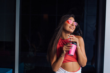 Stylish happy young brunette woman holding pink cup of coffee to go.