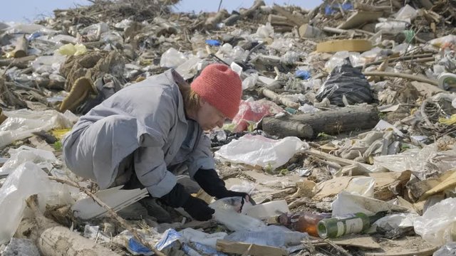 homeless man eats at city dump. bum digs in package of waste in garbage.
