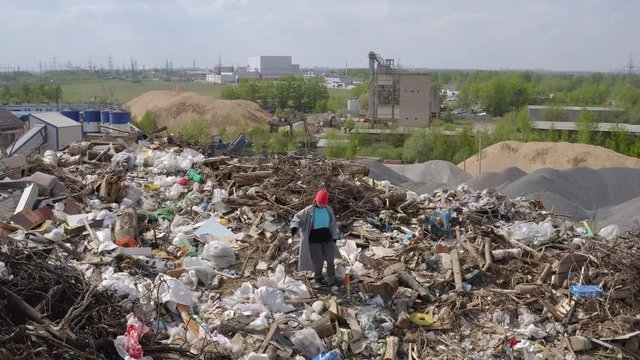 Aerial shot of homeless woman seeking for used things and food at city dump. beggar man walking in trash among waste.