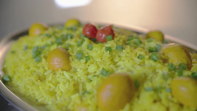 A nice portion of pequi rice served on a medium platter and garnished with red cherry tomatoes and chopped green onions. Typical dish of the Brazilian west center.