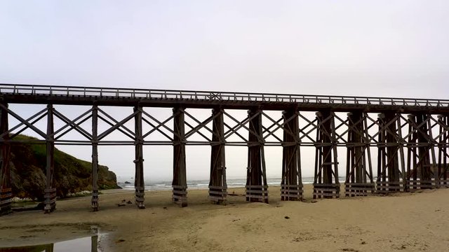 Drone Panning of Pudding Creek Trestle with seashore and waves background. Panoramic view of historical bridge on sand beach.