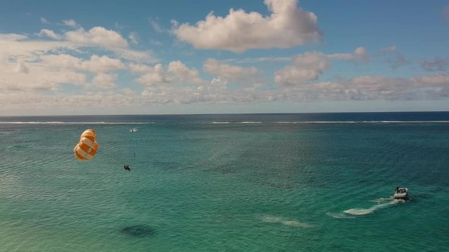 Aerial shot of a couple practicing parasailing. The shot starts whit them touching the water, and then rising