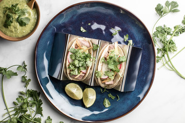 Steak tacos served on homemade tortillas served with grilled onions and tomatillo avocado salsa. garnished with cilantro. served on a blue plate or wooden dish. - 285575658