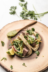 Steak tacos served on homemade tortillas served with grilled onions and tomatillo avocado salsa. garnished with cilantro. served on a blue plate or wooden dish. - 285575675