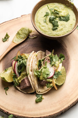 Steak tacos served on homemade tortillas served with grilled onions and tomatillo avocado salsa. garnished with cilantro. served on a blue plate or wooden dish. - 285575696