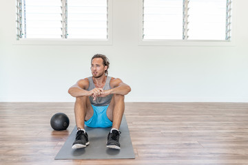 Fit man training exercise at home gym workout with weight medicine ball taking a break sitting on floor tired sweating thinking of weight loss.