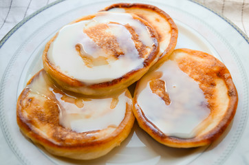 Cottage cheese pancakes, called syrniki, with condensed milk or sweet milk topping on a plate close-up. Traditional breakfast and dessert of Russia, Ukraine, Belarus and CIS countries. 