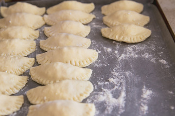 Perogies (varenyky) stuffed and waiting to be boiled on a baking sheet; cooking varenyky from scratch at home in the kitchen