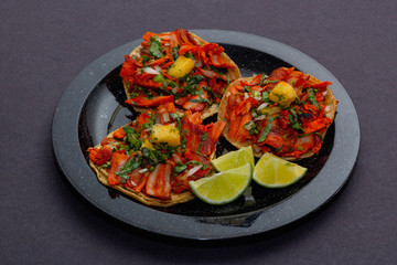 Tacos al pastor de carne de puerco con cilantro, cebolla y piña montados sobre un plato negro