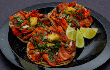 Tacos al pastor de carne de puerco con cilantro, cebolla y piña montados sobre un plato negro